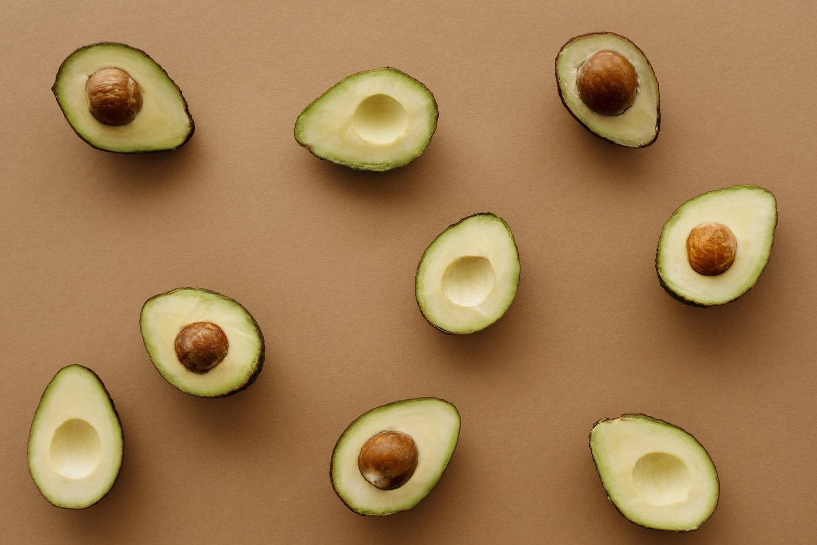 avocado fruits cut in half on brown surface